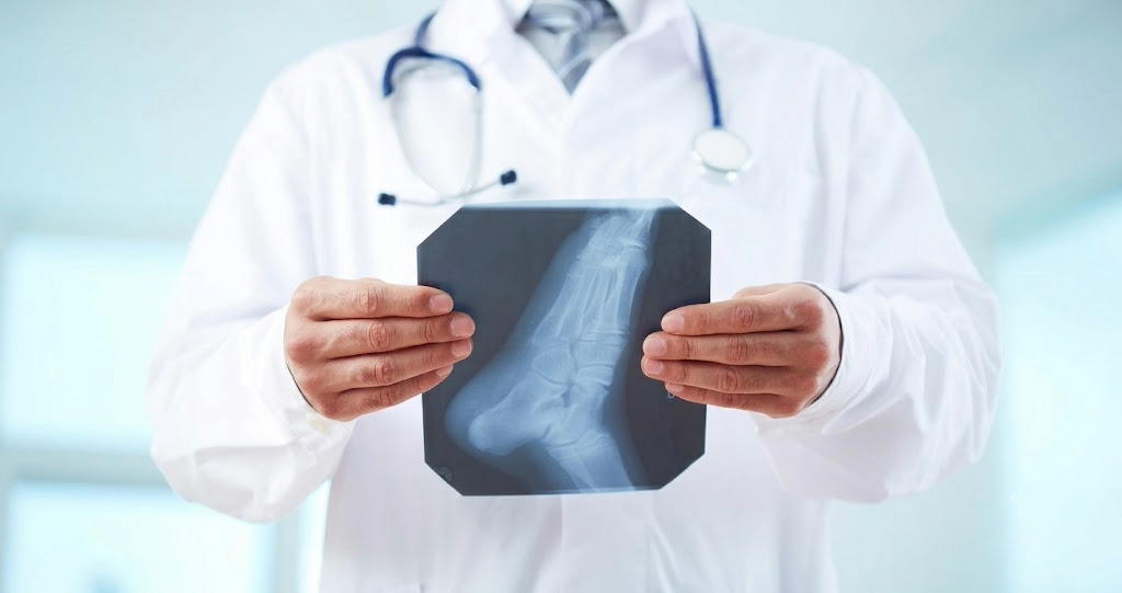 A podiatrist in a white lab coat examining a foot X-ray, highlighting the medical diagnostic capabilities discussed in the comparison between a podiatrist and a chiropodist.