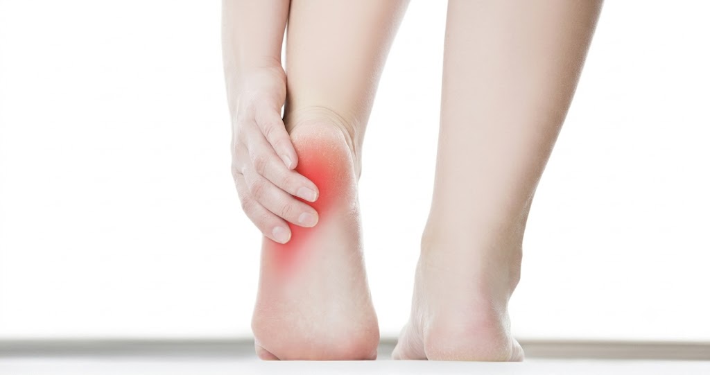 A person massaging their bare heel, with a red highlight illustrating the localized heel pain that is a common symptom of plantar fasciitis.