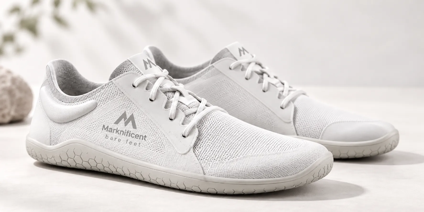 White Marknificent barefoot shoes with a wide toe box, flexible low-profile sole and breathable mesh upper, shown in a minimalist studio product photograph.
